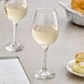 A table with two Acopa all-purpose wine glasses filled with white wine next to a plate of food.