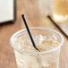 A black EcoChoice PLA straw in a glass on a table with ice and liquid.