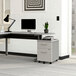A Correll steel mobile pedestal filing cabinet with white laminate drawers under a modern office desk with a computer and a plant on it.