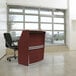 A Correll cherry laminate curved reception desk with a chair in front of it.