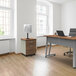 A Correll steel mobile pedestal filing cabinet with walnut laminate drawers under a desk with a laptop on it.