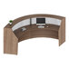 A walnut laminate curved reception desk with a computer and monitor on top.