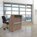 A Correll walnut laminate curved reception counter with a chair in front of it in a room with windows.