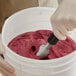 A hand in a glove scooping red Tropical Acai sorbet.
