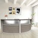 A Correll ash laminate curved reception desk with a glass top.