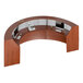 A cherry laminate curved U-shaped reception desk with a computer and phone on it.