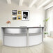 A white Correll reception desk with a curved counter and a white vase with orange flowers on it.