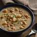 A bowl of Chincoteague New England Clam Chowder with potatoes and herbs next to a spoon.