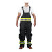 A man wearing Tingley black insulated overalls with reflective stripes over a white shirt.