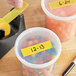 A person uses Lavex yellow masking tape on containers of candy in a school kitchen.