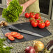 A person cutting tomatoes and lettuce on a Mercer Culinary black composite cutting board on a counter.
