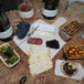 A VerTerra square balsa wood cheese board with a variety of snacks on a wooden table with wine bottles.