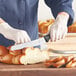 A person using a Mercer Culinary bread knife to cut a loaf of bread on a wooden cutting board.