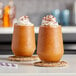 Two glasses of brown Kelvin Slush Co. frozen coffee drinks with whipped cream on top.