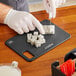 A person cutting food on a Barfly black composite bar board.