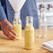 A hand pouring yellow liquid into an 8 oz. PET Ring Neck Sauce Bottle.