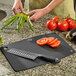 A person cutting vegetables on a Mercer Culinary black composite cutting board.