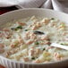 A white bowl of clam chowder with a spoon in it.