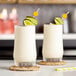 Two glasses of white margarita with lime slices on them.