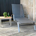 A Three Birds Casual Avanti Teak chaise lounge on a wooden deck with a table and a green potted plant.