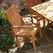 A Three Birds Casual Monterey outdoor wooden dining arm chair next to a table on a patio.