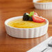 A white Acopa fluted porcelain bowl filled with creme brulee and fruit on a table.