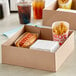 A Kraft paper food tray with a hot dog and fries in it on a table with drinks.