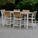 A Three Birds Casual SoHo counter height arm chair with white frame and wood accents at a table with white chairs on a brick patio.