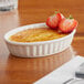 An Acopa ivory fluted porcelain souffle dish filled with creme brulee and strawberries on a table.