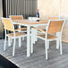 A Three Birds Casual teak square dining table and chairs on a wood deck with wine glasses on the table.