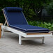 A blue and white Three Birds Casual SoHo Teak chaise lounge chair on a brick patio.