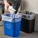 A man's hand throws a crumpled white paper towel into a blue Lavex rectangular trash can.