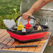 A person holding a red and black Mr. Bar-B-Q picnic basket filled with condiments and sauces.