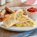 A plate with a Clara's Kitchen Chile Verde Breakfast Burrito and a side of salsa on a white surface.