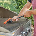 A person cleaning a grill with a Mr. Bar-B-Q Triple-Action Grill Brush.