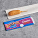A State Fair Classic corn dog on a stick on a table next to a bag of bread rolls.