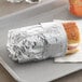 A sandwich wrapped in Bagcraft silver honeycomb foil on a tray.