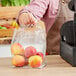 A person's hand using a Choice clear plastic soft loop bag to hold a bag of apples.