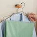 A hand holding a green shirt on a Choice heavy-duty metal hanger.