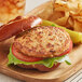 A close-up of a Before the Butcher plant-based chicken patty on a wooden plate with lettuce and tomato.