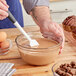 A person using a spatula to mix Lindt milk chocolate with other ingredients in a bowl.