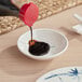 A person pouring sauce into a bowl on a table using an Acopa Biru sauce dish.
