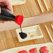 A hand pouring soy sauce into an Acopa Brassia rectangular sauce dish on a table.