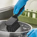 A person in blue gloves using an Advantage Supplies black floating utility/pot scrub brush to clean a pan.