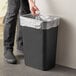 A person putting a plastic bag into a black Lavex rectangular trash can.