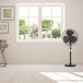 A VisionAir black pedestal fan in a room with a window.