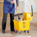 A person using a Lavex mop bucket with casters to mop the floor.
