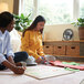 A group of women sitting on the floor in a room with a VisionAir black USB table fan.