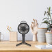 A black VisionAir handheld fan on a table next to a plant.