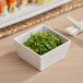 A white Acopa Bambu melamine bowl filled with green seaweed salad on a table in an Asian cuisine restaurant.